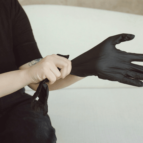 A cropped image featuring a person wearing a black t-shirt putting on a black medical/latex glove.