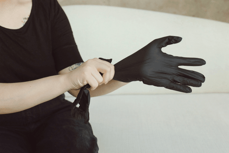 A cropped image featuring a person wearing a black t-shirt putting on a black medical/latex glove.